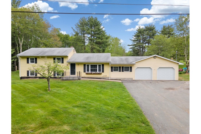 Tri-level home featuring driveway, an attached garage, a front yard, and view of wooded area