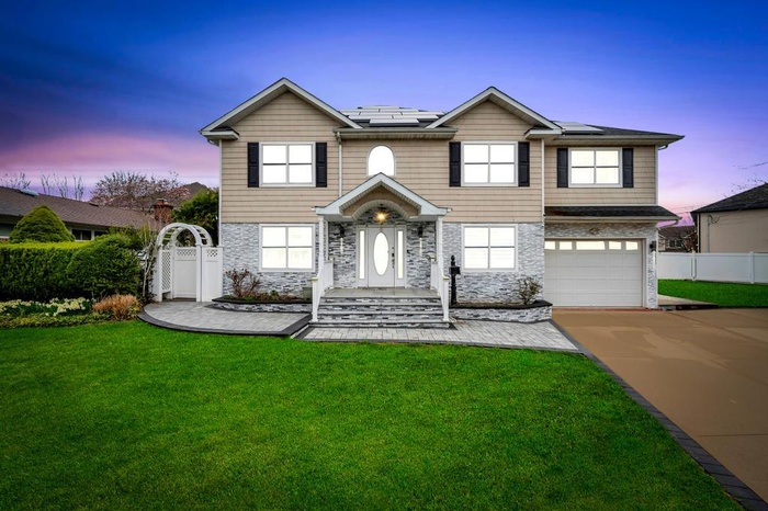 Traditional-style house featuring an attached garage, stone siding, fence, a front lawn, and driveway