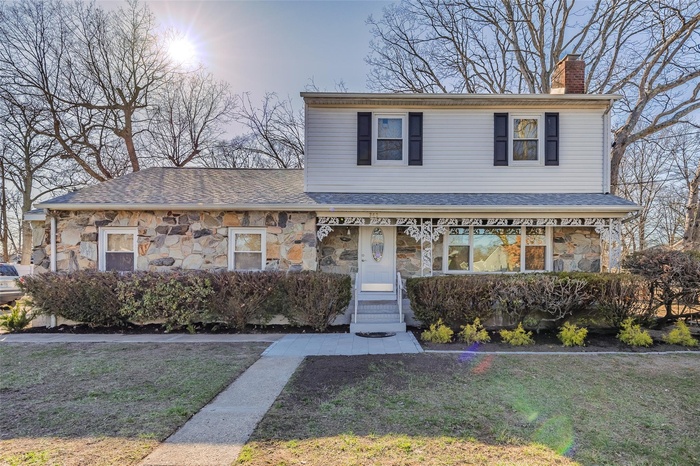 View of front facade with stone siding, a chimney, a front yard, roof with shingles, and a porch