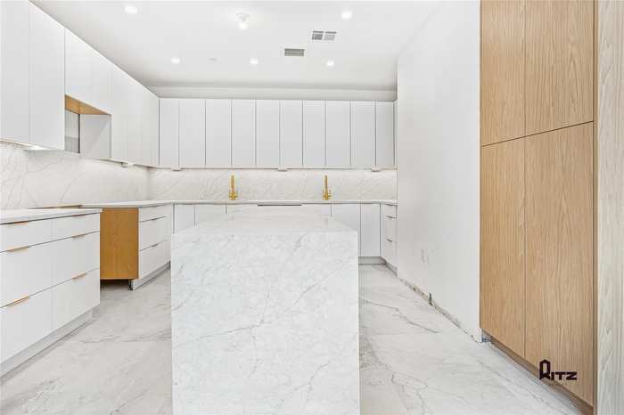 Kitchen featuring tasteful backsplash, light stone counters, a center island, and white cabinets