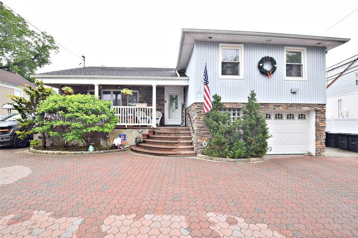 View of front of home featuring stone siding, covered porch, a garage, and driveway