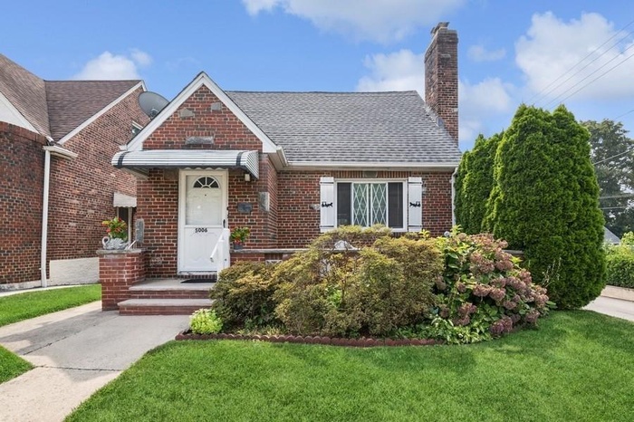 View of front of home with brick siding, a front yard, a chimney, and roof with shingles