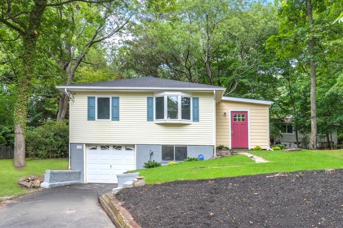 View of front of property with driveway, an attached garage, a front yard, and view of wooded area