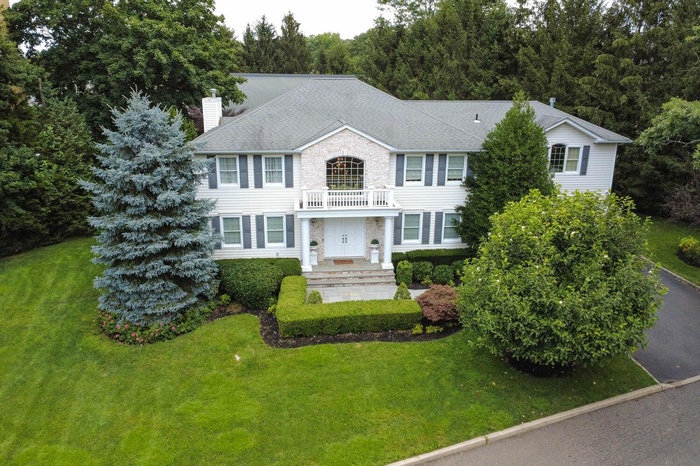 Colonial home with a balcony, a chimney, a front lawn, and roof with shingles