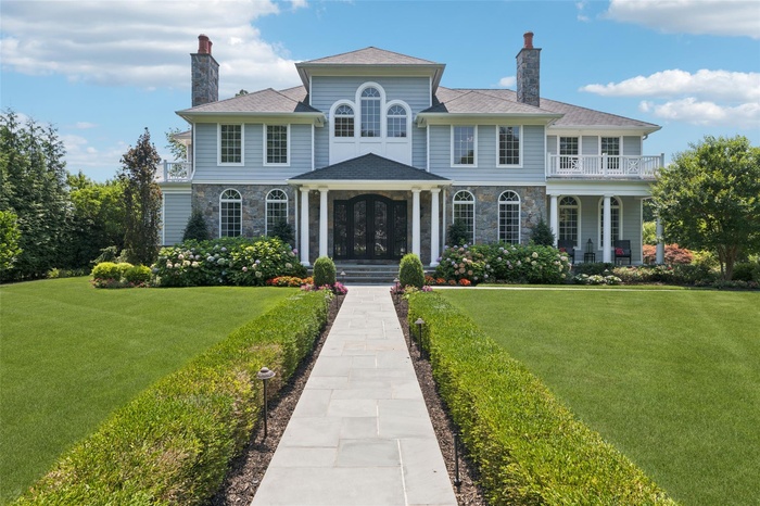 View of front of home with a chimney, stone siding, a balcony, and a front lawn