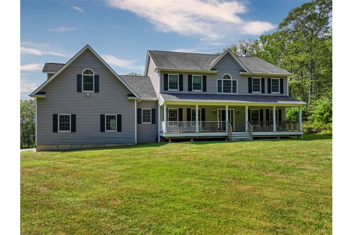View of front of house with a shingled roof, covered porch, and a front yard
