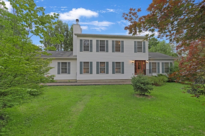 Colonial home with a front yard and mature landcaping for privacy