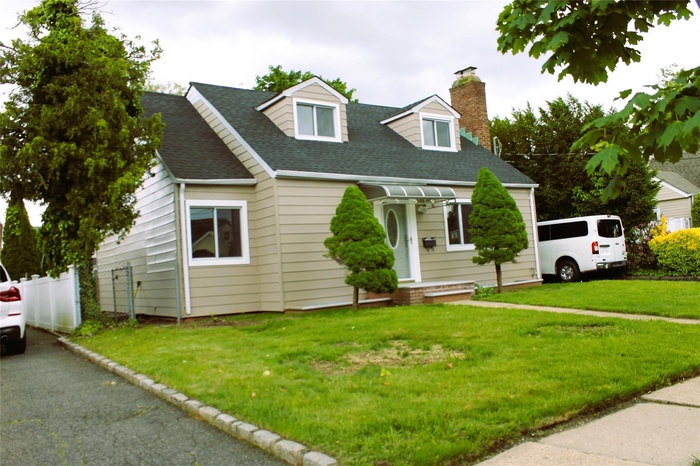 Cape cod home with a chimney, a front lawn, and roof with shingles