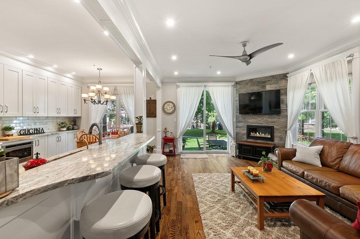 Living room with a large fireplace, dark wood-style flooring, ornamental molding, a ceiling fan, and a chandelier