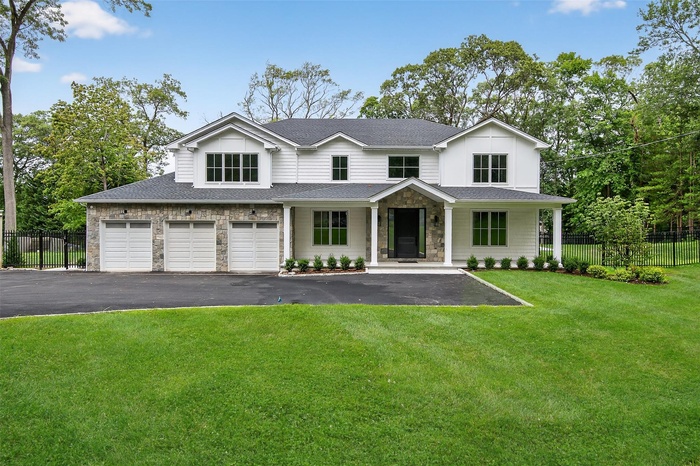 View of front of home with asphalt driveway, a garage, stone siding, covered porch, and a shingled roof