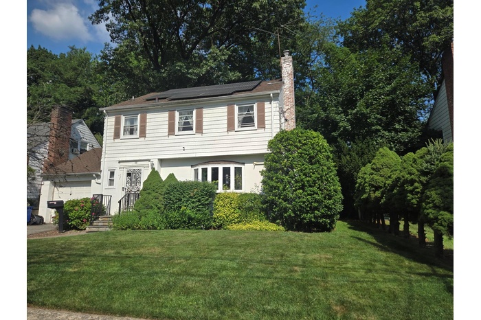 View of front of home featuring a chimney, roof mounted solar panels, a front yard,