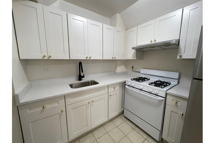 Kitchen with white range with gas stovetop, under cabinet range hood, white cabinetry, light tile patterned floors, and light stone counters