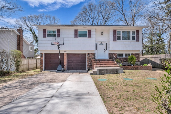 Raised ranch with fence, concrete driveway, brick siding, and a garage