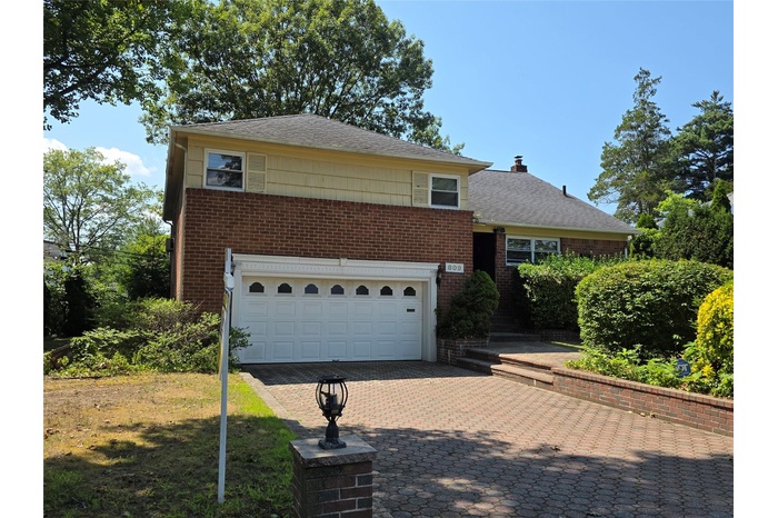 View of front of home with an attached garage, decorative driveway, brick siding, and roof with shingles