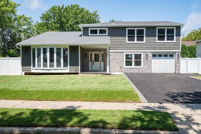 View of front of house featuring driveway, a shingled roof, an attached garage, and stone siding