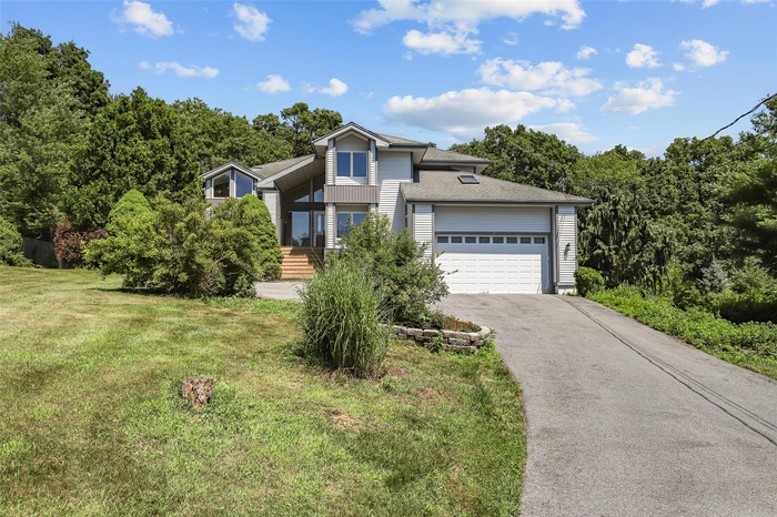 View of front of property featuring an attached garage, asphalt driveway, a front lawn, a shingled roof, and a view of trees