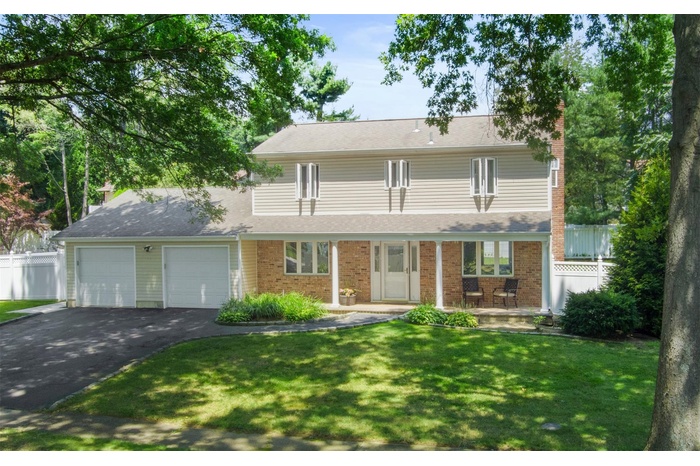 Traditional-style house with asphalt driveway, a garage, a chimney, brick siding, and covered porch