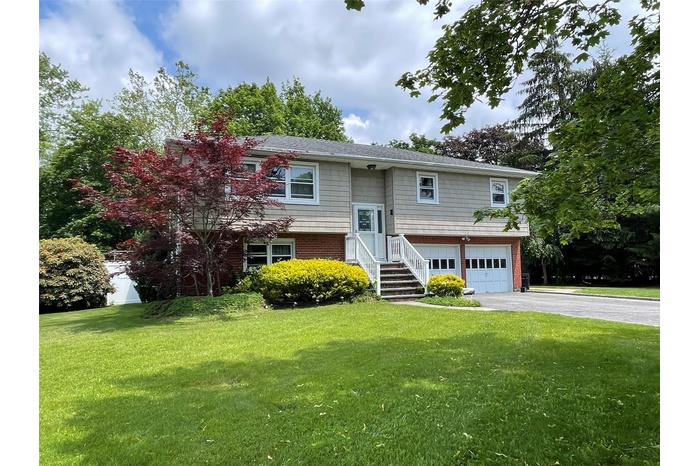 Raised ranch featuring asphalt driveway, a garage, a front yard, and brick siding