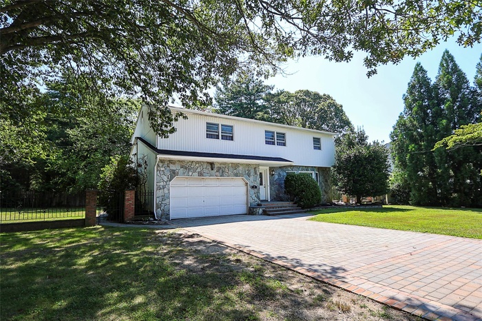 View of front of home featuring an attached garage, stone siding, and decorative driveway