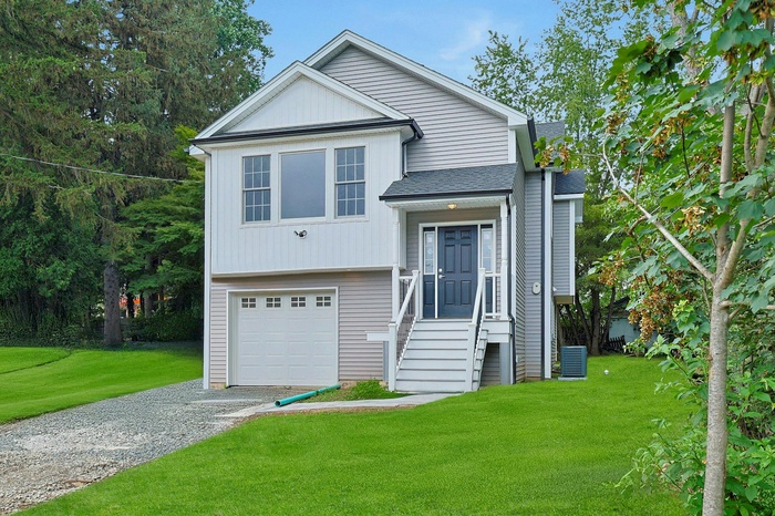 View of front of property featuring a front yard, gravel driveway, a shingled roof, and an attached garage