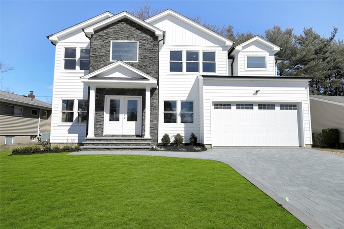 View of front of house with decorative driveway, a front lawn, stone siding, board and batten siding, and an attached garage