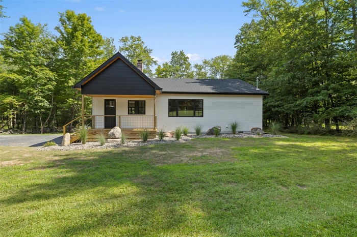 View of front facade featuring covered porch, a front lawn, and a chimney