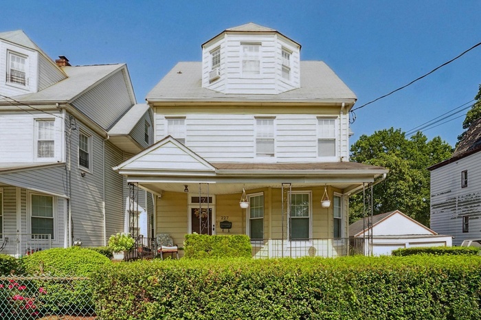 View of front of home with a porch, roof with shingles, and a garden style front yard