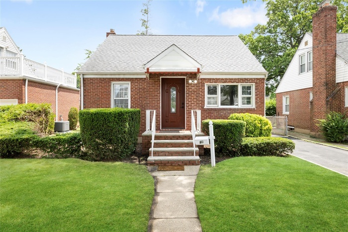 View of front of home with brick siding, a front lawn, and roof with shingles