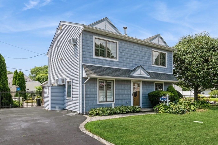 View of front of house with a shingled roof and an AC wall unit