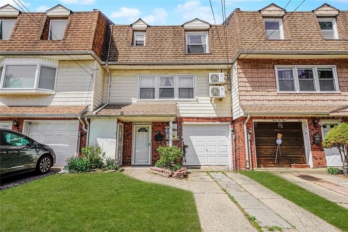 Multi unit property featuring an attached garage, brick siding, roof with shingles, and a front yard