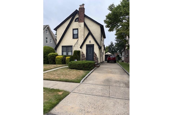 View of front facade with a chimney, stucco siding, driveway, and cooling unit