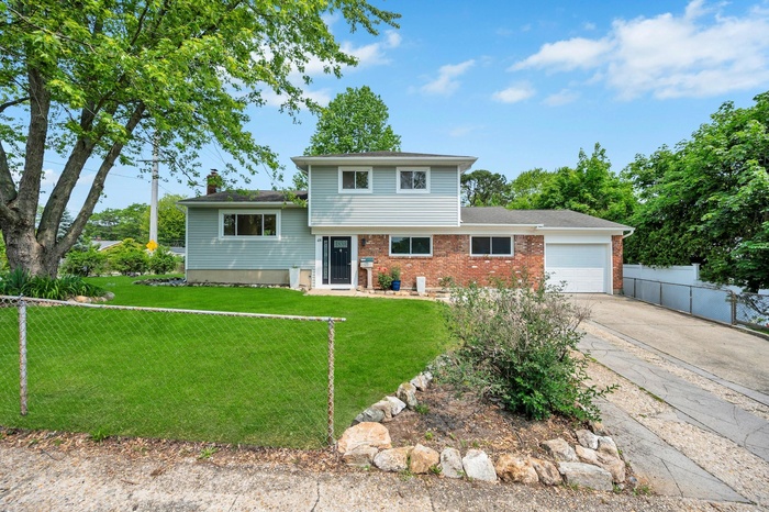 Tri-level home featuring an attached garage, brick siding, concrete driveway, roof with shingles, and a chimney
