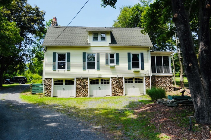 View of front of property featuring stone siding, a chimney, roof with shingles, and a sunroom