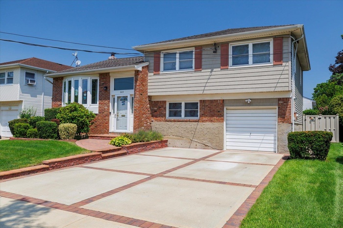 Tri-level home featuring concrete driveway, an attached garage, brick siding, and a front lawn