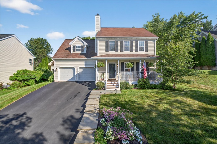 View of front facade featuring covered porch, a garage, asphalt driveway, a chimney, and a front yard