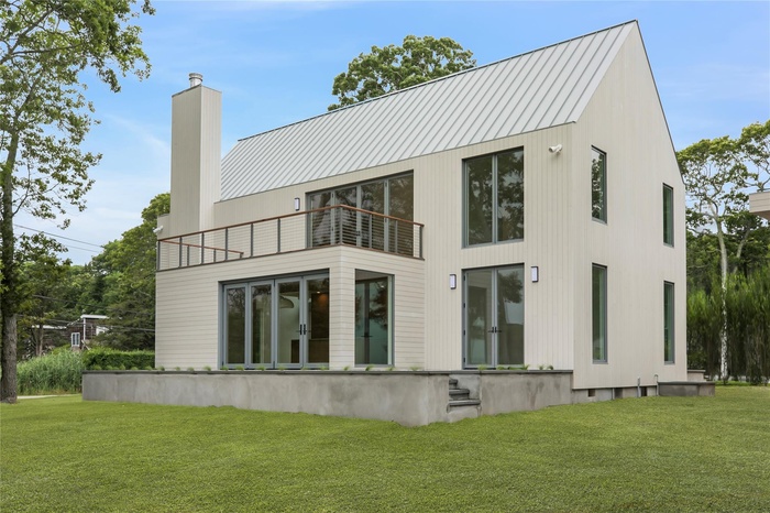 Back of property with a balcony, a chimney, a lawn, and a standing seam roof