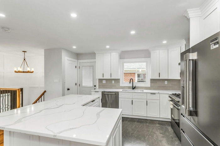 Kitchen with high end appliances, a chandelier, a kitchen island, white cabinets, and tasteful backsplash