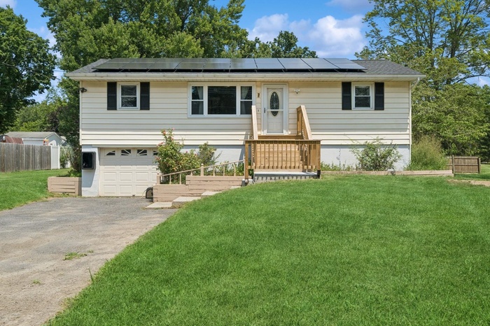 Single story home featuring asphalt driveway, solar panels, and a garage
