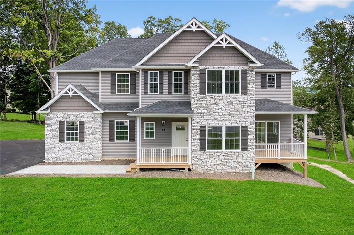 Front of the house with stone siding, a lawn, a shingled roof, and covered porch