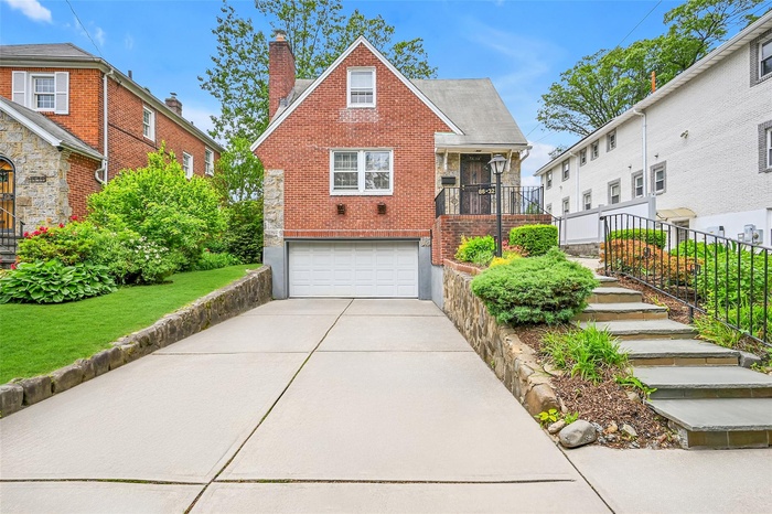 View of front of home with a garage, brick siding, concrete driveway, a chimney, and stairs