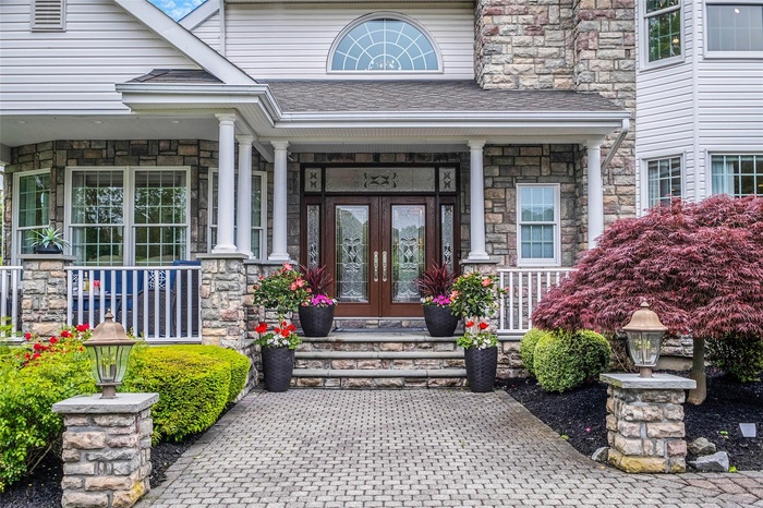Doorway to property with french doors, stone siding, a porch, and roof with shingles