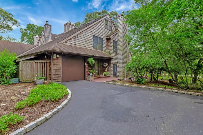 View of front of home featuring a chimney, driveway, a garage, and roof with shingles