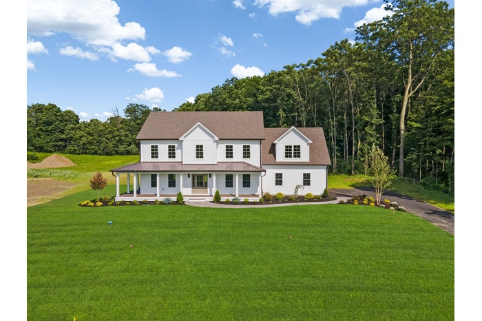 View of front facade with a porch, a front yard, a metal roof, and a forest view
