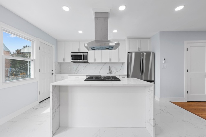 Kitchen with island range hood, appliances with stainless steel finishes, recessed lighting, light marble finish floors, and backsplash