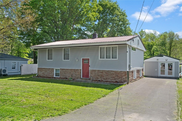 Split foyer home with french doors, brick siding, a chimney, a front yard, and metal roof