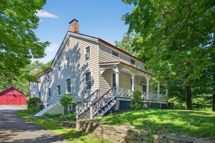 View of front of house with covered porch, a chimney, an outdoor structure, a garage, and a front lawn