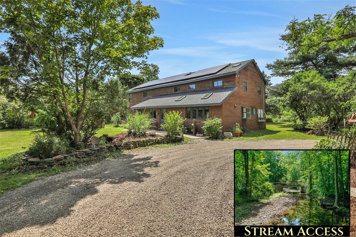 Rustic home featuring a front lawn, roof mounted solar panels, dirt driveway, roof with shingles, and view of wooded area