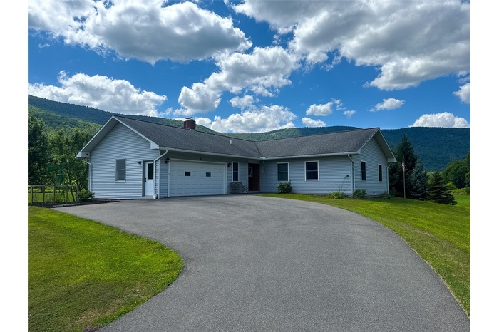 Ranch-style home featuring a garage, driveway, a front lawn, and a mountain view