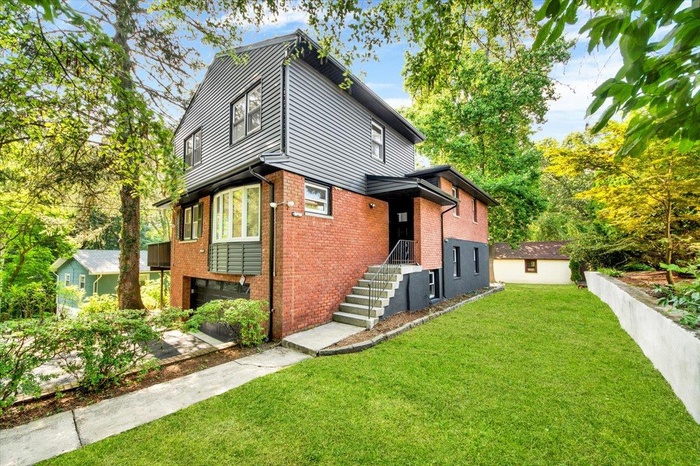 Rear view of property featuring brick siding, a lawn, a garage, and driveway