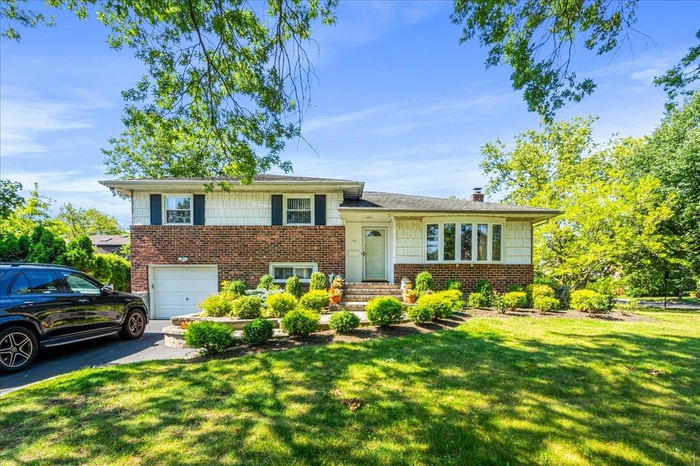 Tri-level home with brick siding, a front lawn, driveway, and an attached garage